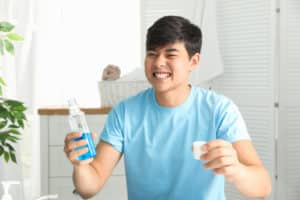 Man holding bottle and cap with mouthwash in bathroom. 