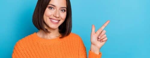 A cheerful girl in bright orange knitted sweater demonstrating a empty hand copy space sign